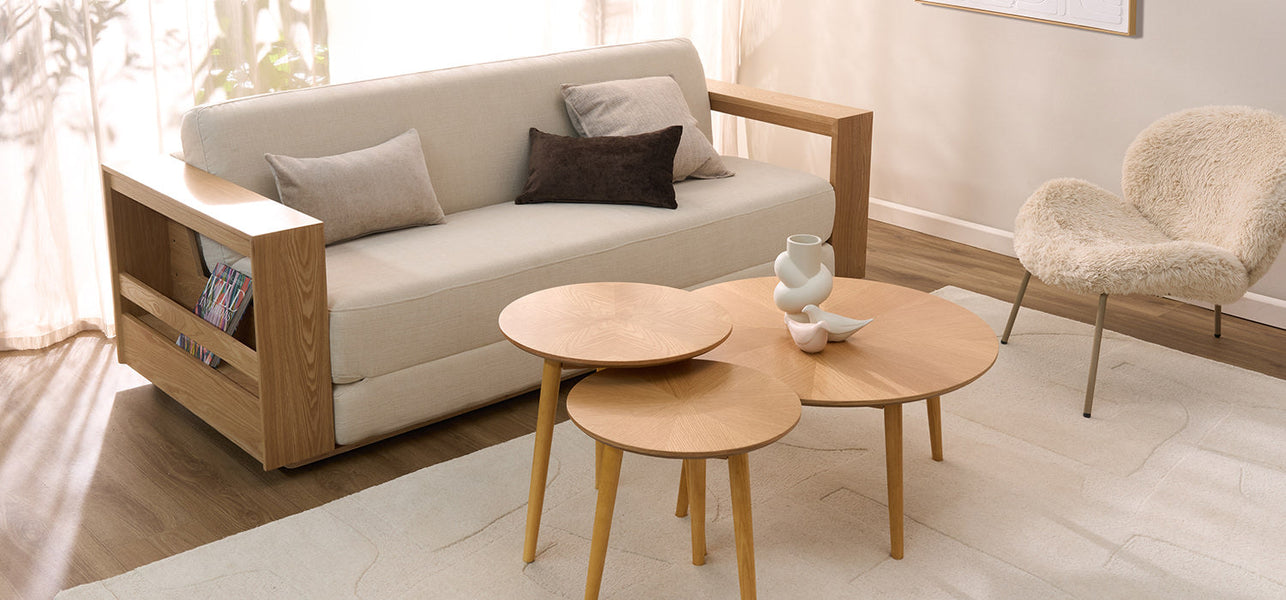 Smoked-ash-coloured round coffee table with two glases and a little sculpture on top in a modern living room, with a soft-fabric sofa in the background. 