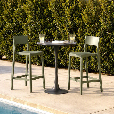 A 3-piece outdoor bar set featuring a round black pedestal table and two olive green barstools, arranged on a concrete patio next to a swimming pool with a green hedge in the background.