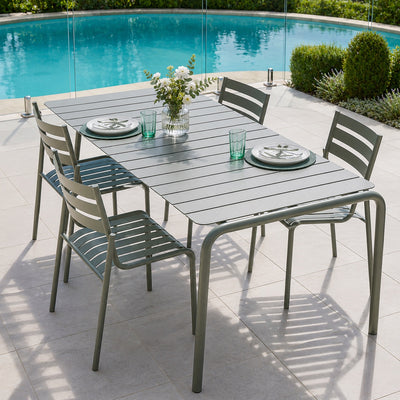 An outdoor dining set consisting of a rectangular gray slatted table and four matching gray chairs, arranged on a light stone patio next to a swimming pool.