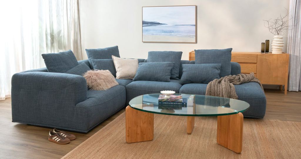 Modern living room with a blue sectional sofa, glass coffee table, and wooden sideboard.